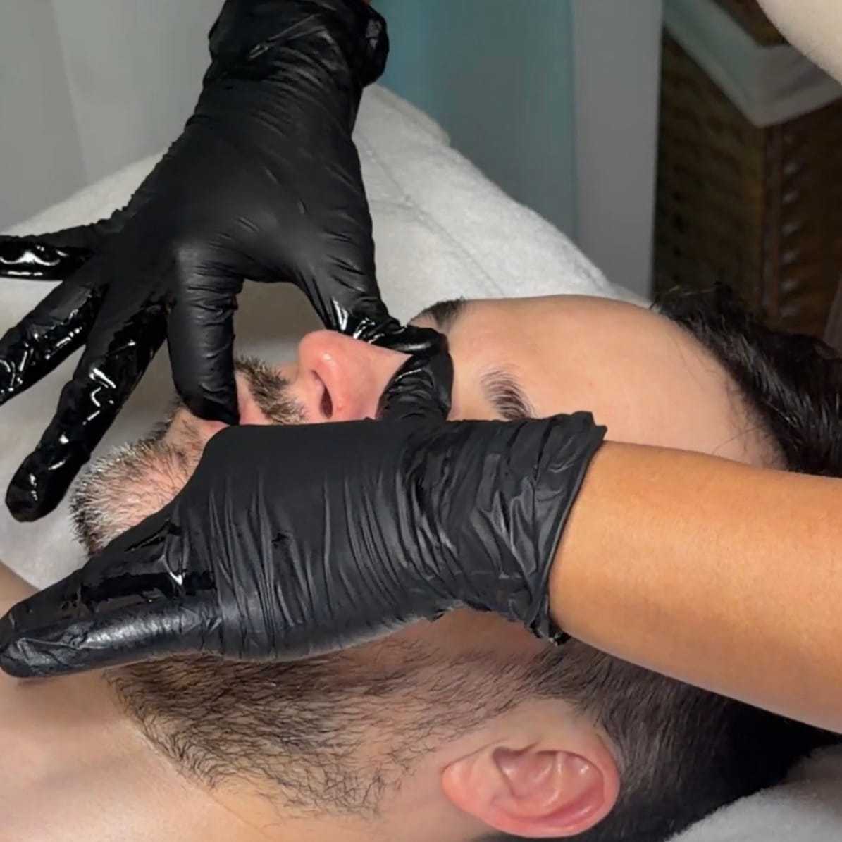 Man receiving a facial massage with black gloves in a spa setting.