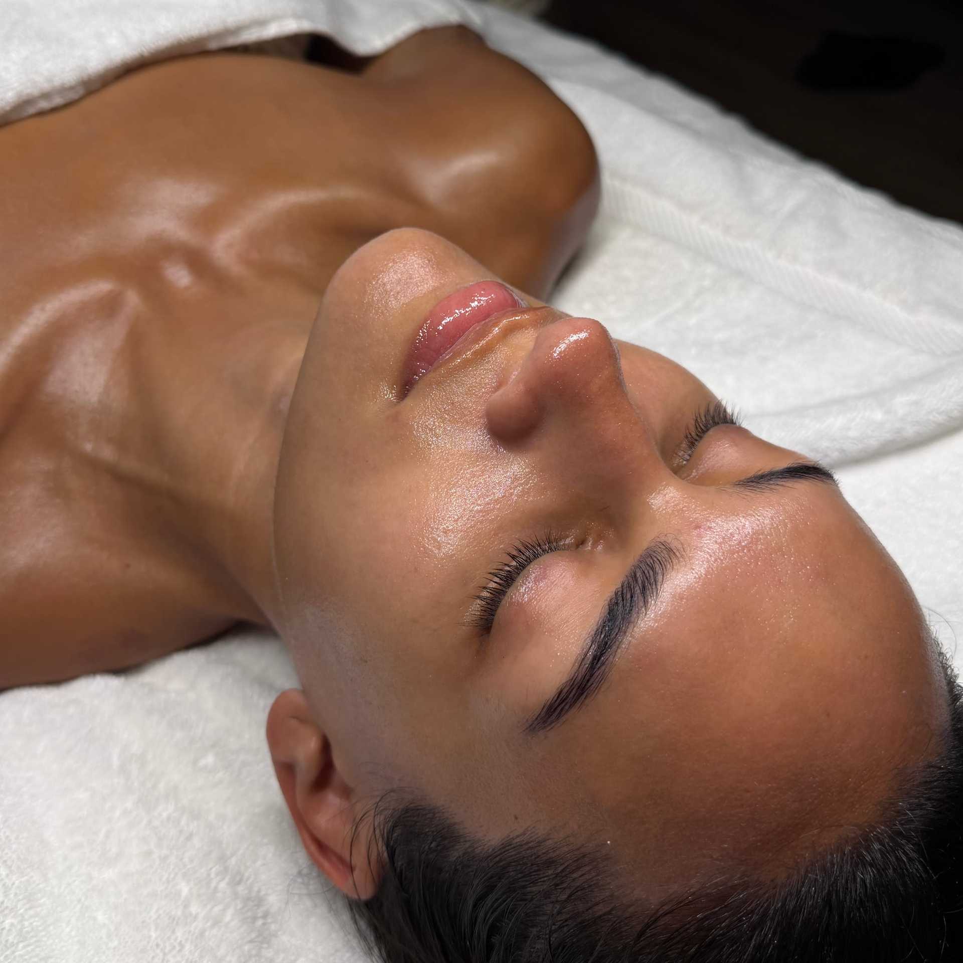 Person relaxing during a spa treatment, lying on a white towel, eyes closed.