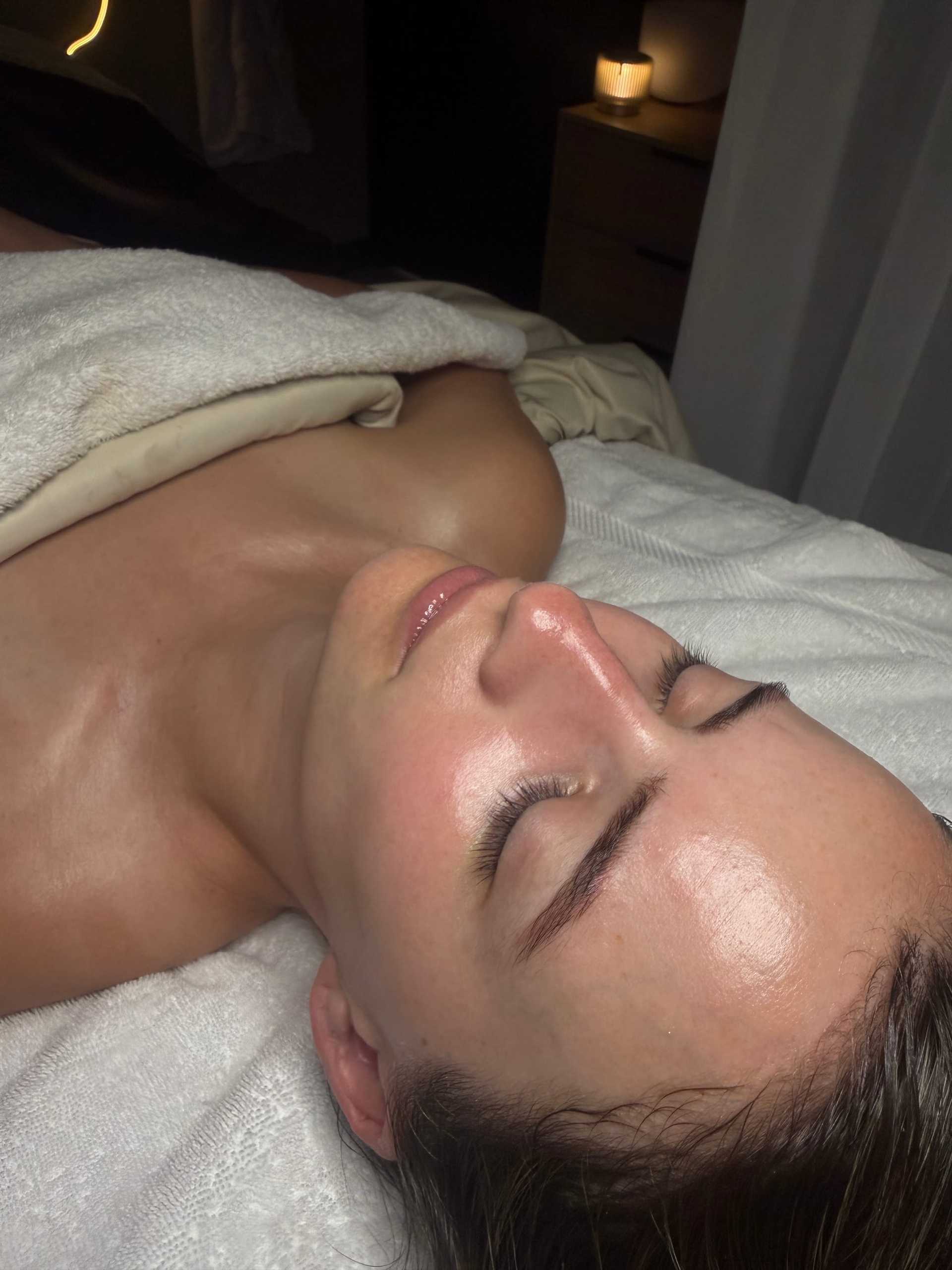 Person relaxed on a massage table with closed eyes and a lit candle nearby.